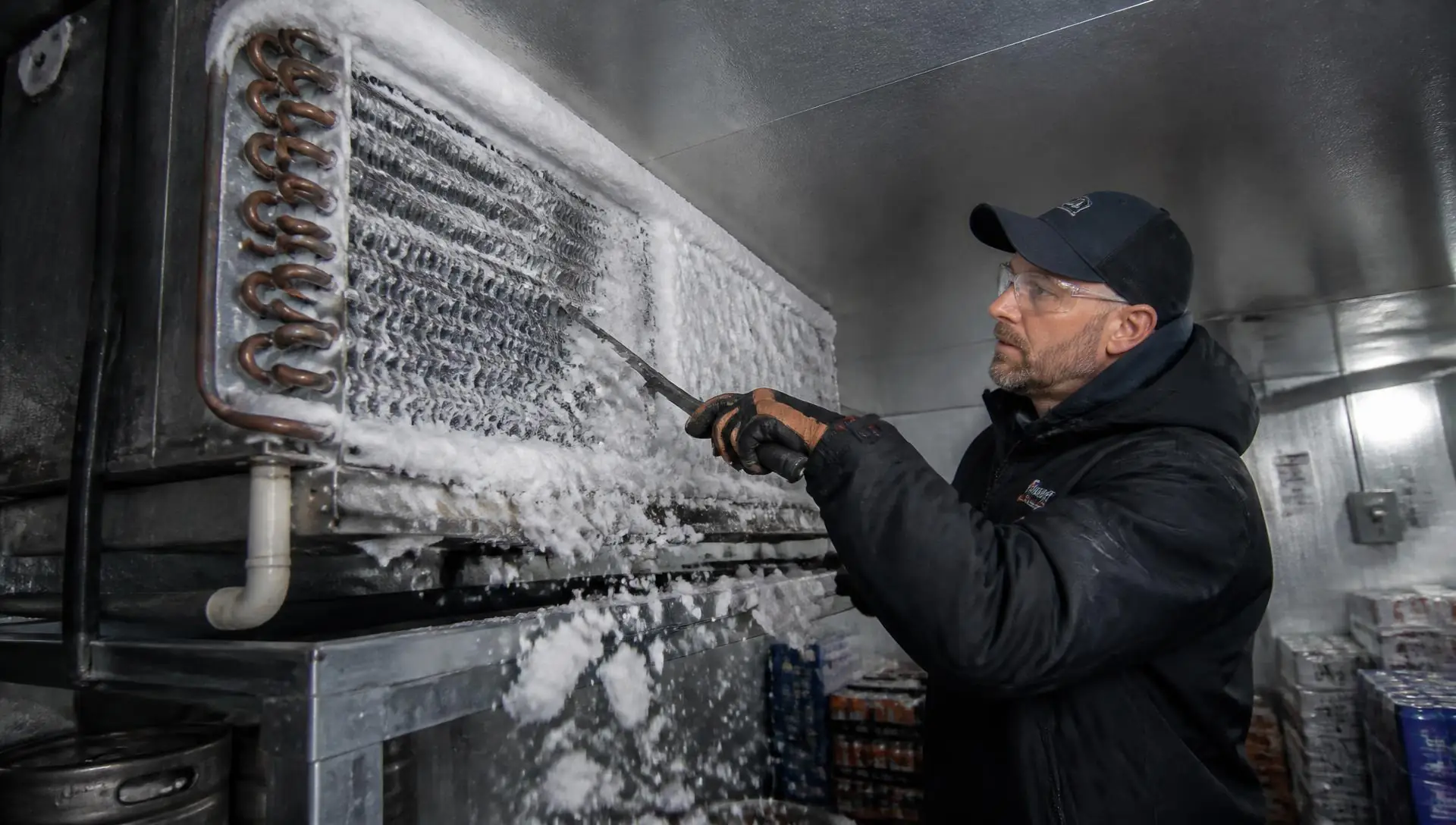 Refrigeration technician removing ice from a frozen evaporator coil in a walk-in cooler